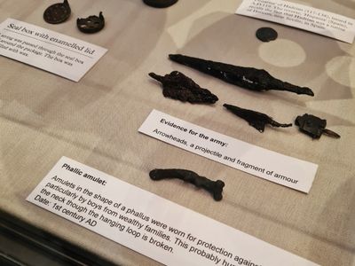 A collection of metal arrowheads, seals and amulets in a glass case