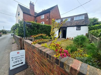 White cottage with flower garden and a sign in front saying Roman Site and Museum Open