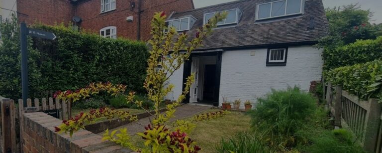 White cottage with flower garden and a sign in front saying Museum