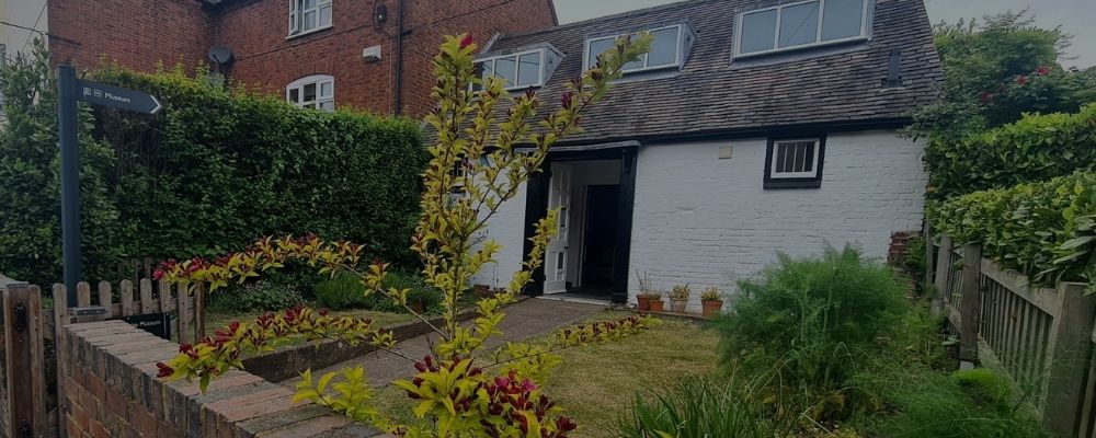 White cottage with flower garden and a sign in front saying Museum